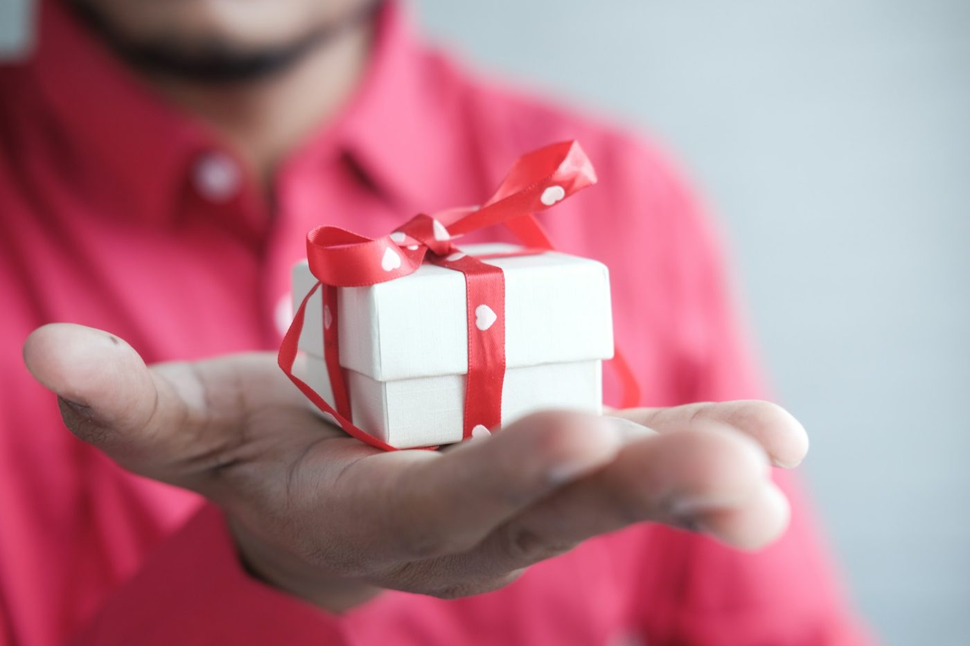 Main tendue offrant un petit paquet cadeau au ruban rouge